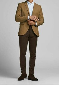 Hnědý vypasovaný blazer přes světle modrou košili, doplněný o tmavě hnědé úzké kalhoty a odpovídající semišové boty. Jednoduchý a elegantní design.