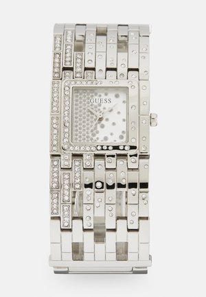 Montre en métal argenté avec un cadran rectangulaire, des accents en cristal et un bracelet texturé présentant des largeurs variées et des strass intégrés.