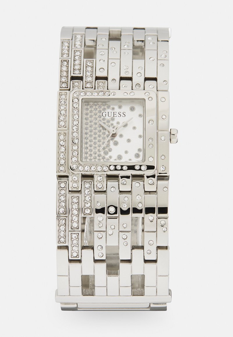 Montre en métal argenté avec un cadran rectangulaire, des accents en cristal et un bracelet texturé présentant des largeurs variées et des strass intégrés.