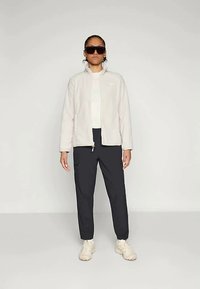 Jasnoszara polarowa kurtka z zamkiem błyskawicznym na przodzie, noszona na białej bluzce, w połączeniu z ciemnymi spodniami z bocznymi kieszeniami na zamek i jasnymi sneakersami.