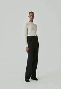 Long-sleeve ribbed cream top paired with high-waisted black wide-leg trousers, featuring a smooth texture and minimalistic design.