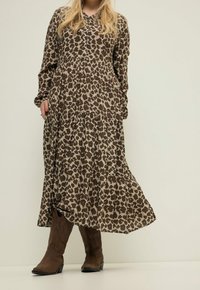 Robe à imprimé léopard marron et beige avec manches longues, design à volants et détails boutonnés, associée à des bottes de cowboy marron.