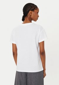 T-shirt bianco in cotone con vestibilità classica, maniche corte arrotolate e colletto tondo. Il retro è semplice, senza grafiche o decorazioni.