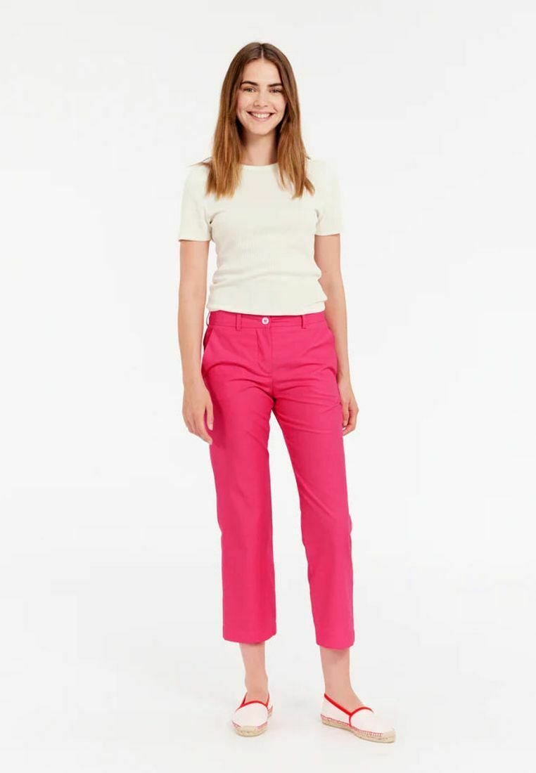 Un pantalon en coton rose à coupe droite, associé à un haut à manches courtes côtelé de couleur beige clair et des espadrilles blanches avec des accents rouges.