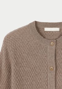Beige stickad cardigan med diamantstruktur, rund halsringning och två knappar. Tyget verkar mjukt med en subtil glans från materialet.