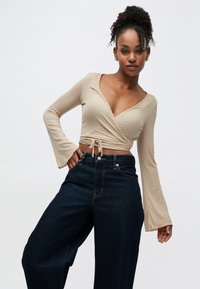 Bēšas krāsas kamzolis ar garām zvana formas piedurknēm, kas sasienams jostasvietā. Kombinēts ar tumši ziliem, platiem džinsiem ar augstu jostasvietu.