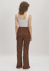 Bruine geribde wijde broek met elastische tailleband, gecombineerd met een aansluitend wit tanktop, dat een eenvoudige, casual uitstraling laat zien.
