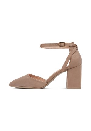 Beżowy zamszowy but na wysokim obcasie z zaostrzonym noskiem i paskiem wokół kostki. Posiada obcas typu słupek oraz minimalistyczny design.