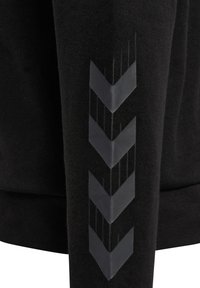 Manche en tissu noir avec quatre bandes en chevron gris foncé orientées vers le bas imprimées verticalement le long du bras.