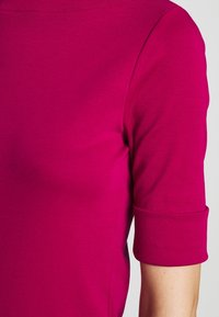 Fuksia puuvillapaita lyhyillä hihoilla. Hihoissa on käänteet. Sujuva pinta yksinkertaisella, klassisella muotoilulla ilman lisäkuvioita.