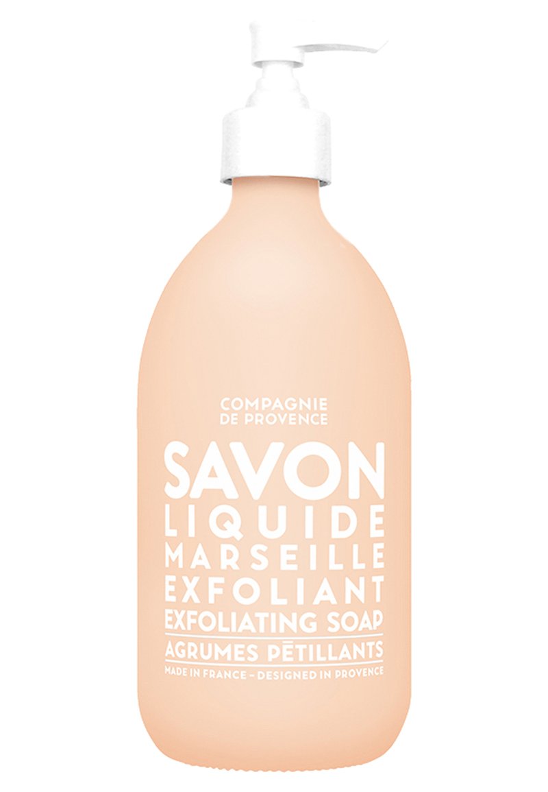 Bouteille rose de savon exfoliant avec une pompe blanche, présentant un texte blanc en gras. Texture lisse, forme arrondie et design minimaliste.