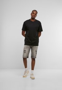 Czarny t-shirt z krótkim rękawem, w połączeniu z jasnoszarymi, zniszczonymi szortami dżinsowymi oraz beżowymi sportowymi butami z białymi akcentami. Prosty, casualowy strój.