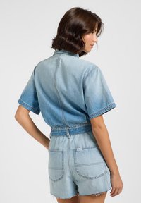 Denim jumpsuit i ljusblått, korta ärmar, med bälte i midjan, två bakfickor och fransad fåll på shortsen. Slät textur med urblekt mönster.