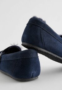 Pantofole in suede blu navy con una morbida fodera in pelliccia, profilo basso e suola in gomma testurizzata. Presentano dettagli di cucitura e un design minimalista.