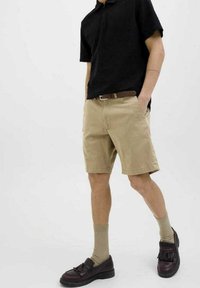 Shorts khaki a taglio dritto, abbinati a una polo nera a maniche corte e scarpe scure. Calzini beige aggiungono texture e contrasto.