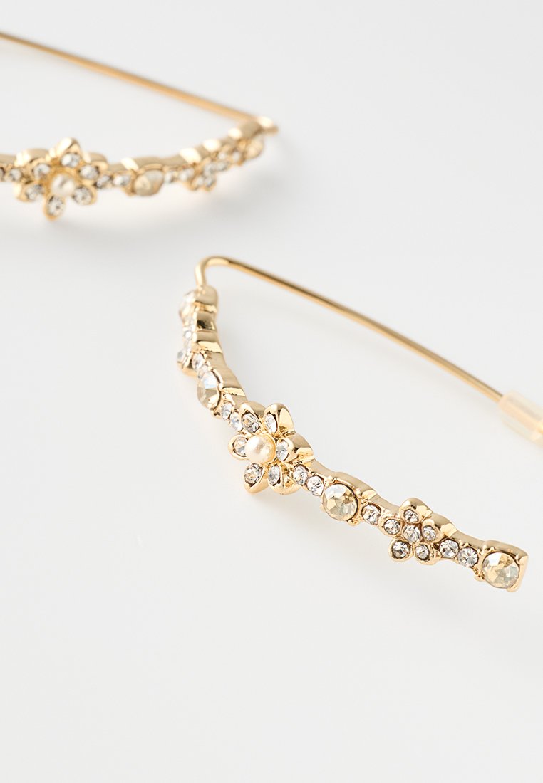 Goldfarbene Ohrringe mit floralen Designs, verziert mit klaren Strasssteinen und einem Perlenakzent. Geschwungene Form mit strukturierter Oberfläche.