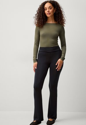 Langärmliges olivgrünes Oberteil kombiniert mit schwarzen Schlaghosen. Das Outfit zeichnet sich durch ein figurbetontes Design und einen glatten, dehnbaren Stoff aus.