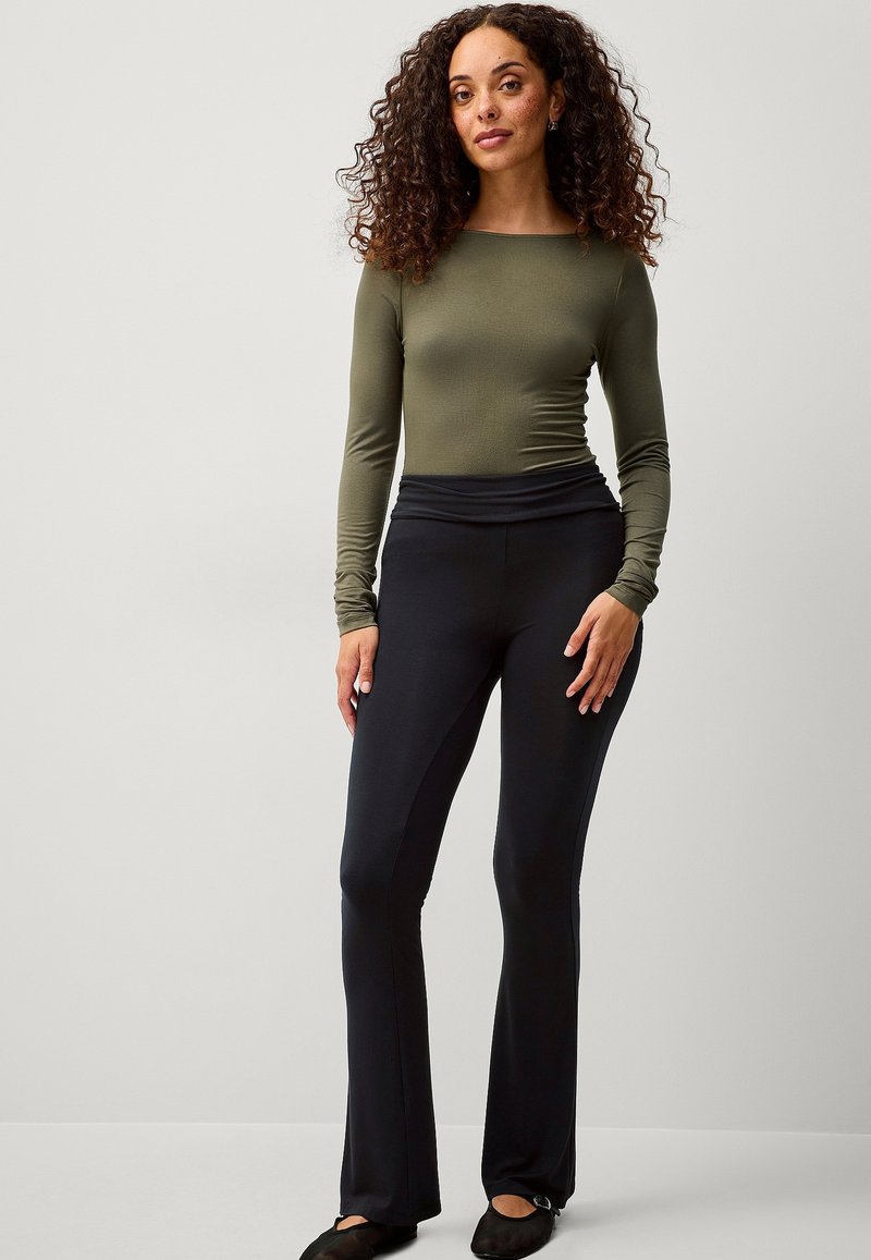 Lange mouwen olijfgroen top gecombineerd met zwarte flared pants. De outfit heeft een fitted ontwerp en een soepele, rekbare stof.