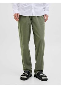 Pantalones de color verde oliva, holgados, hechos de una tela ligera con una textura suave. Llevados con sandalias negras de doble tira.