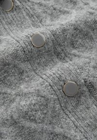 Grey knit fabric with a textured pattern, featuring smooth grey buttons with a gold rim, highlighting softness and warmth.