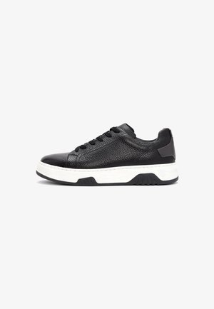Black textured leather low-top sneaker with black laces and thick white sole with black tread on white background.