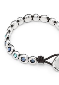 Bracelet en argent composé de maillons en forme d'ovale, alternant avec des pierres précieuses rondes et scintillantes en bleu et turquoise, maintenu avec un cordon noir.