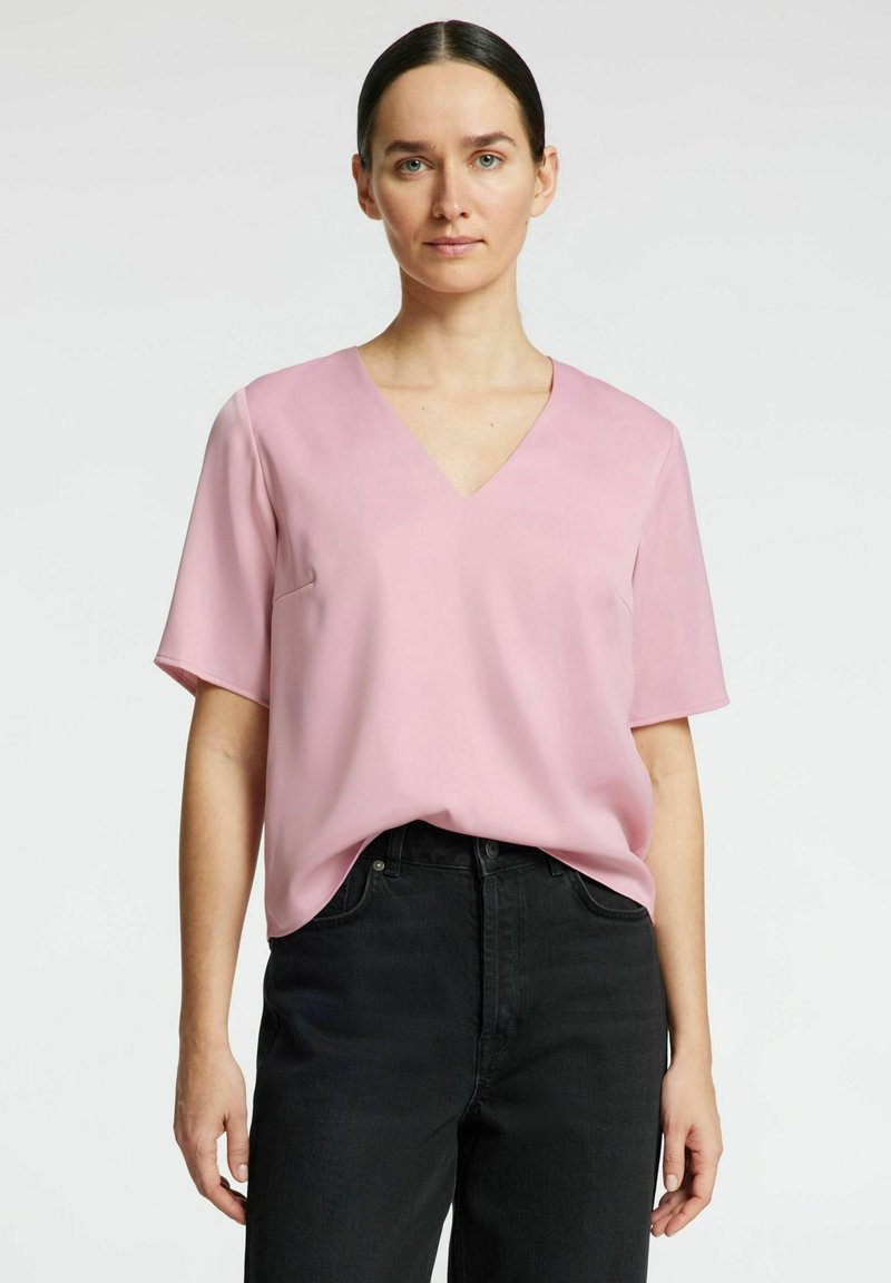 Blusa de color rosa claro con escote en forma de V y mangas cortas, de textura suave y corte holgado, combinada con unos pantalones vaqueros negros de talle alto.