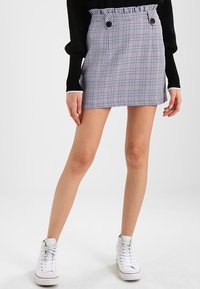 Tkaná minisukně s černobílým kostkovaným vzorem, s volánkovým páskem v oblasti pasu, dvěma knoflíky a slim fit, doplněná o bílé tenisky.