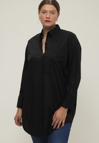 Chemise noire à boutons avec manches longues, dotée d'une poche poitrine, d'un ourlet incurvé et d'une légère brillance. Fabriquée en tissu doux en mélange de coton.