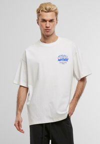 Hvit bomulls oversized t-skjorte med blå grafisk trykk på venstre bryst, korte ermer og rund hals.