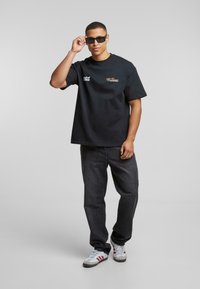 Svart bomulls t-skjorte med en avslappet passform, med hvite og gull logoer. Sammen med mørk denim jeans og grå sneakers med røde striper.