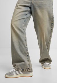 Faded blue straight-leg jeans with visible stitching details, paired with gray suede sneakers featuring white stripes and a rubber sole.