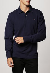 Navyblaues Langarm-Polohemd aus Baumwolle, mit einem umgeschlagenen Kragen, einer Knopfleiste mit zwei Knöpfen und einem kleinen gestickten Logo auf der Brust.