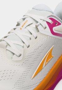 Λευκό αθλητικό παπούτσι με λευκά κορδόνια, πορτοκαλί και ροζ λεπτομέρειες, με την ένδειξη "TORIN 8" στη γλώσσα και το λογότυπο "ALTRA" στο πλάι.