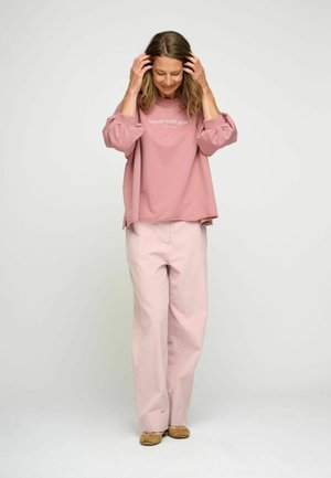 Felpa rosa con la scritta "fiorisci con grazia", abbinata a pantaloni a gamba larga di un rosa chiaro. Tessuto morbido, vestibilità comoda e maniche leggermente a sbuffo.