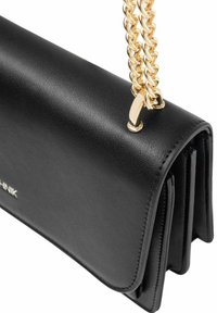 Czarna skórzana torba na ramię z złotym łańcuszkiem, o stonowanej formie, gładkiej fakturze i zamknięciu na klapkę. Widoczne logo na przodzie.