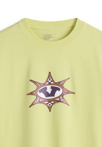 Limetkově zelené tričko s kulatým grafickým motivem v oranžové, fialové a černé kostkované vzoru, ve středu je stylizované logo "V".