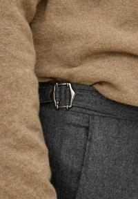 Brun stickad tröja kombinerad med grå ullbyxor, med en silverfärgad metallspänne som har en särskild form och design detaljer.