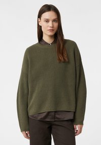 Olivgrüner, gerippter Strickpullover mit rundem Ausschnitt, überschnittenen Schultern und langen Ärmeln. Getragen über einem braunen Hemd mit Kragen und dunkler Hose.