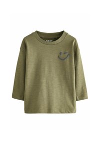 Chemise à manches longues vert olive avec un décolleté rond et un graphisme d'emoji souriant en gris sur le côté gauche de la poitrine. Tissu doux et texturé.