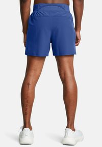 Pantalones cortos deportivos azules con una textura suave, cinturilla elástica y un pequeño bolsillo trasero, usados con zapatillas blancas y tatuajes de pierna visibles.