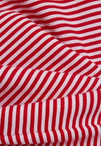 Gros plan d'un tissu doux et plié avec des rayures étroites rouges et blanches horizontales tricotées créant un motif texturé.