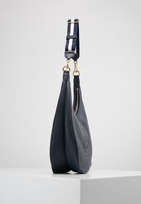 Marinblå läderväska med en strukturerad yta, prydd med en guldfärgad dragkedja och ett randigt textilhandtag i marinblått och vitt. Kurvad siluett.