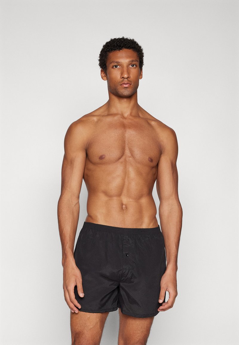 Schwarze Badeshorts mit elastischem Bund, ausgestattet mit einem Knopfverschluss vorne und einer leichten, glatten Textur.