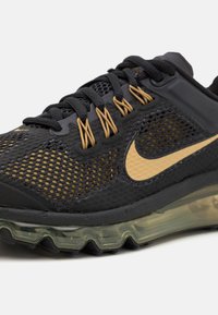 Μαύρο αθλητικό παπούτσι με επάνω μέρος από πλέγμα, χρυσές λεπτομέρειες και ορατή σόλα με αερο cushioning. Διαθέτει υφή και πλεχτό κορδόνι.