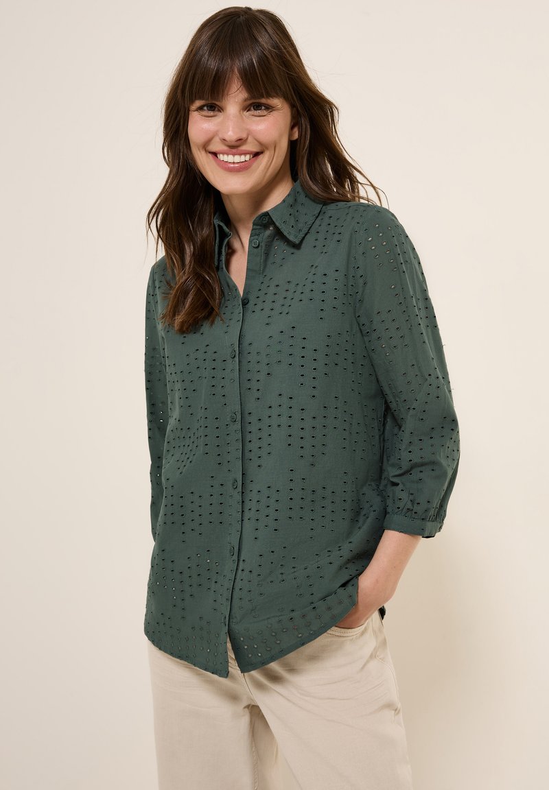 Chemise verte à manches trois-quarts, dotée de détails perforés et d'un col structuré. Tissu léger avec une texture lisse.