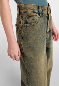 Ljusblå högmidjade denimjeans med en urblekt tvätt, framfickor och dragkedja. Tyget har en strukturerad yta med synliga sömmar.