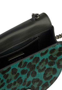 Czarna skórzana torebka z turkusowym wnętrzem w wzór geparda, z wystającym srebrnym łańcuchem i eleganckim, zgeometryzowanym kształtem.