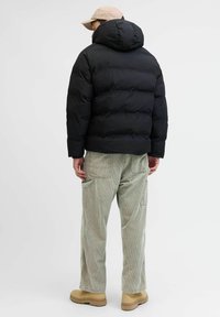 Svart dunjakke med hette, med et quiltet design. Brukt med lysegrønne kordfløyelsbukser og beige støvler. Enkel og funksjonell silhuett.