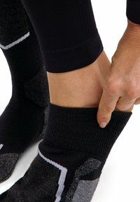 Czarne i szare skarpetki sportowe z żebrowanymi mankietami i geometrycznymi wzorami. Materiał wydaje się teksturowany, odpowiedni dla komfortu i wsparcia.